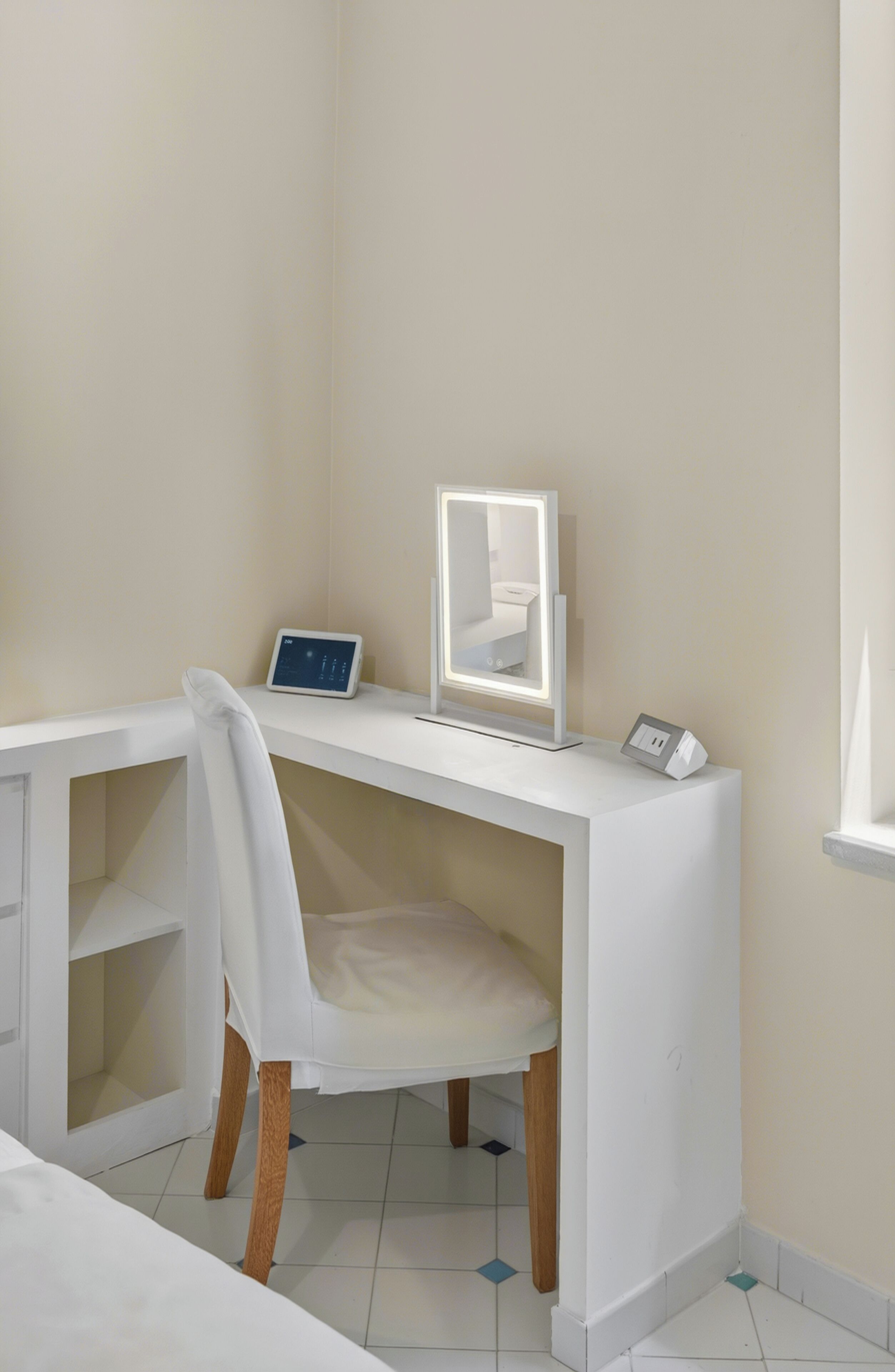 A white desk with a mirror, a digital clock, and a power strip.