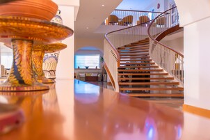 A spacious interior with a polished wooden staircase, a large vase, and a dining area with chairs.