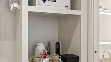 A white storage unit with a coffee maker, cups, a kettle, and a small appliance on the shelves.