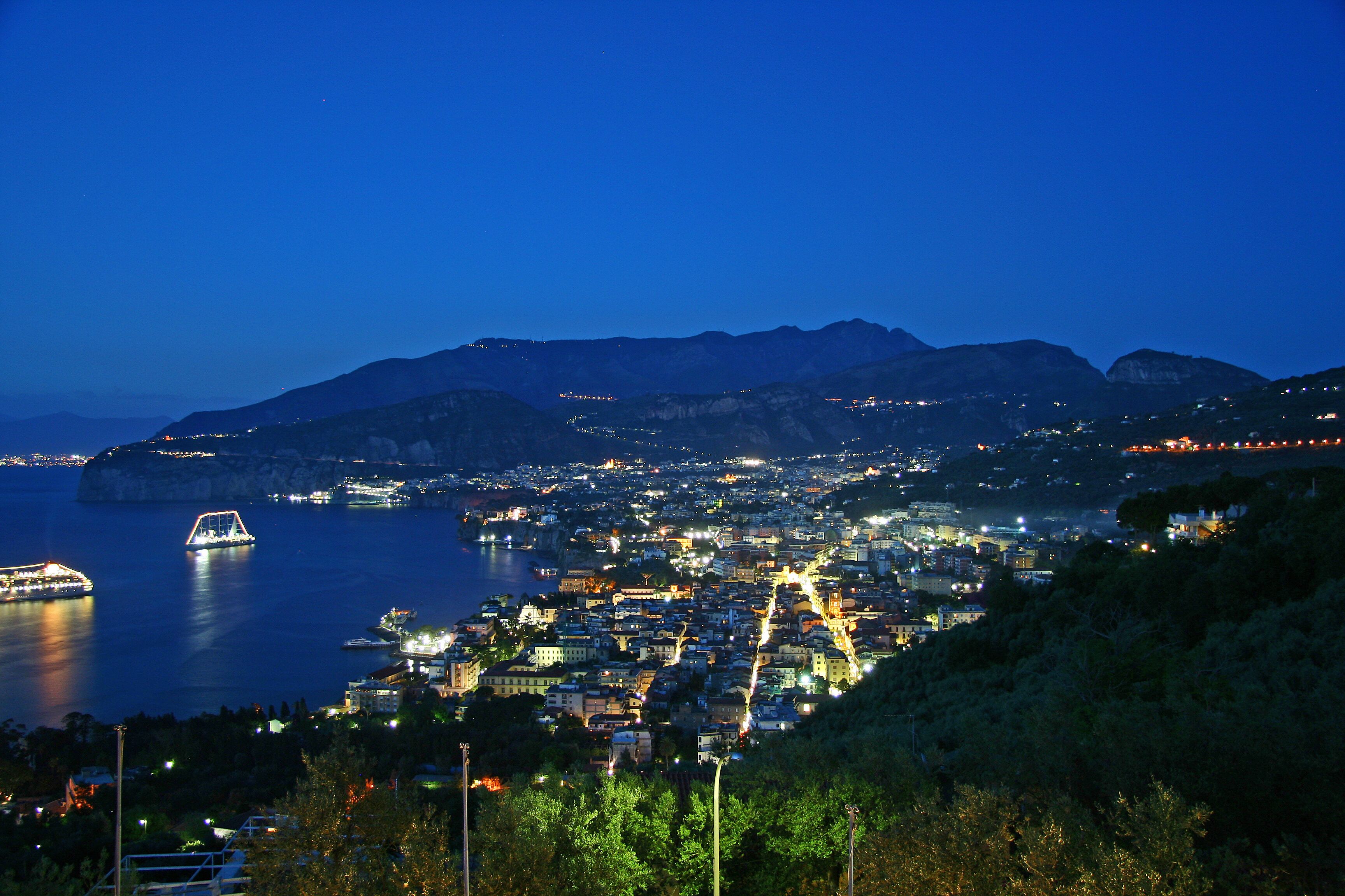 A coastal city at night with illuminated buildings and a bridge over the water.