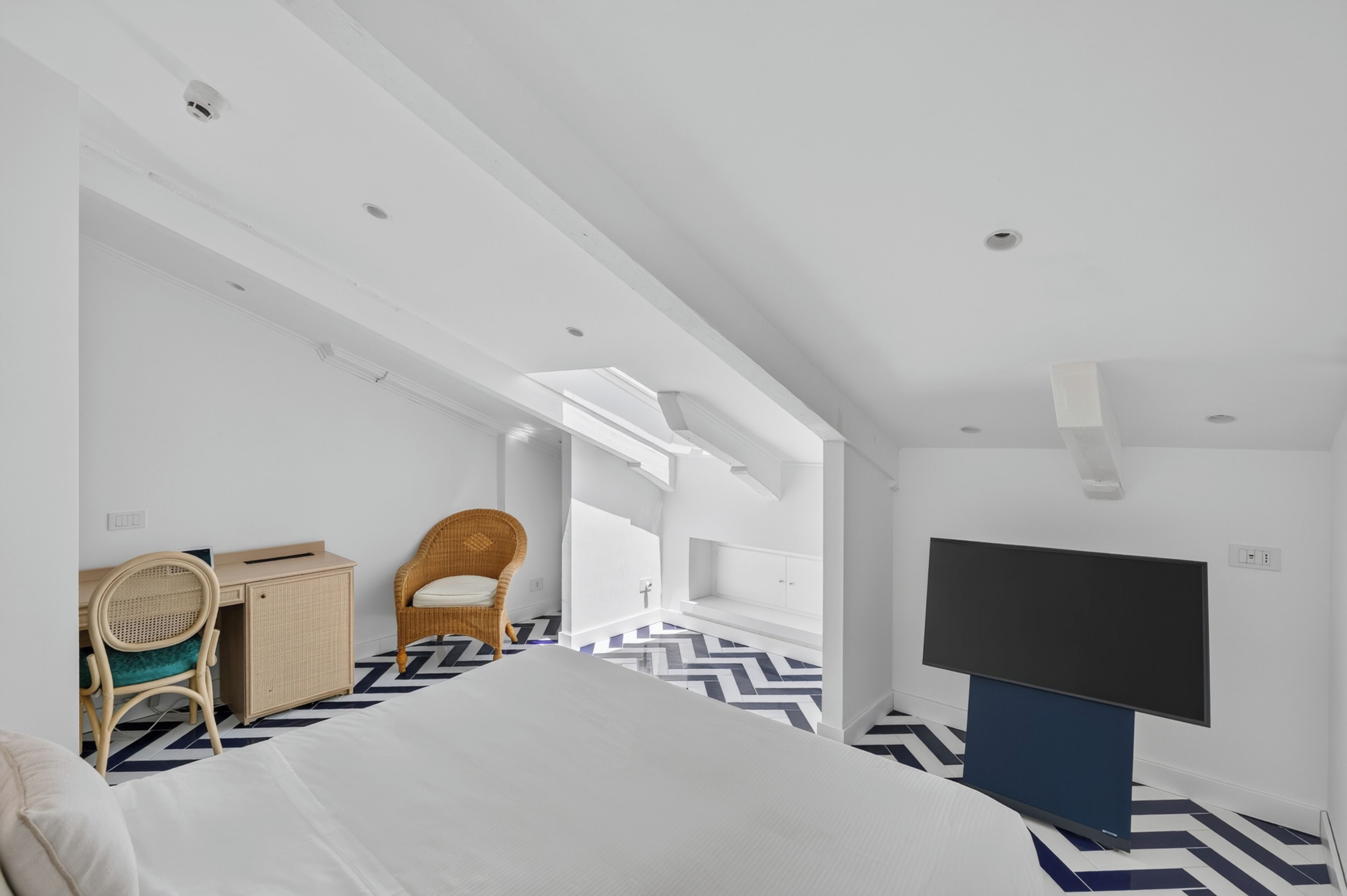 Een moderne hotelkamer met een bed, een bureau, een stoel, een televisie en een visgraatvloer.
