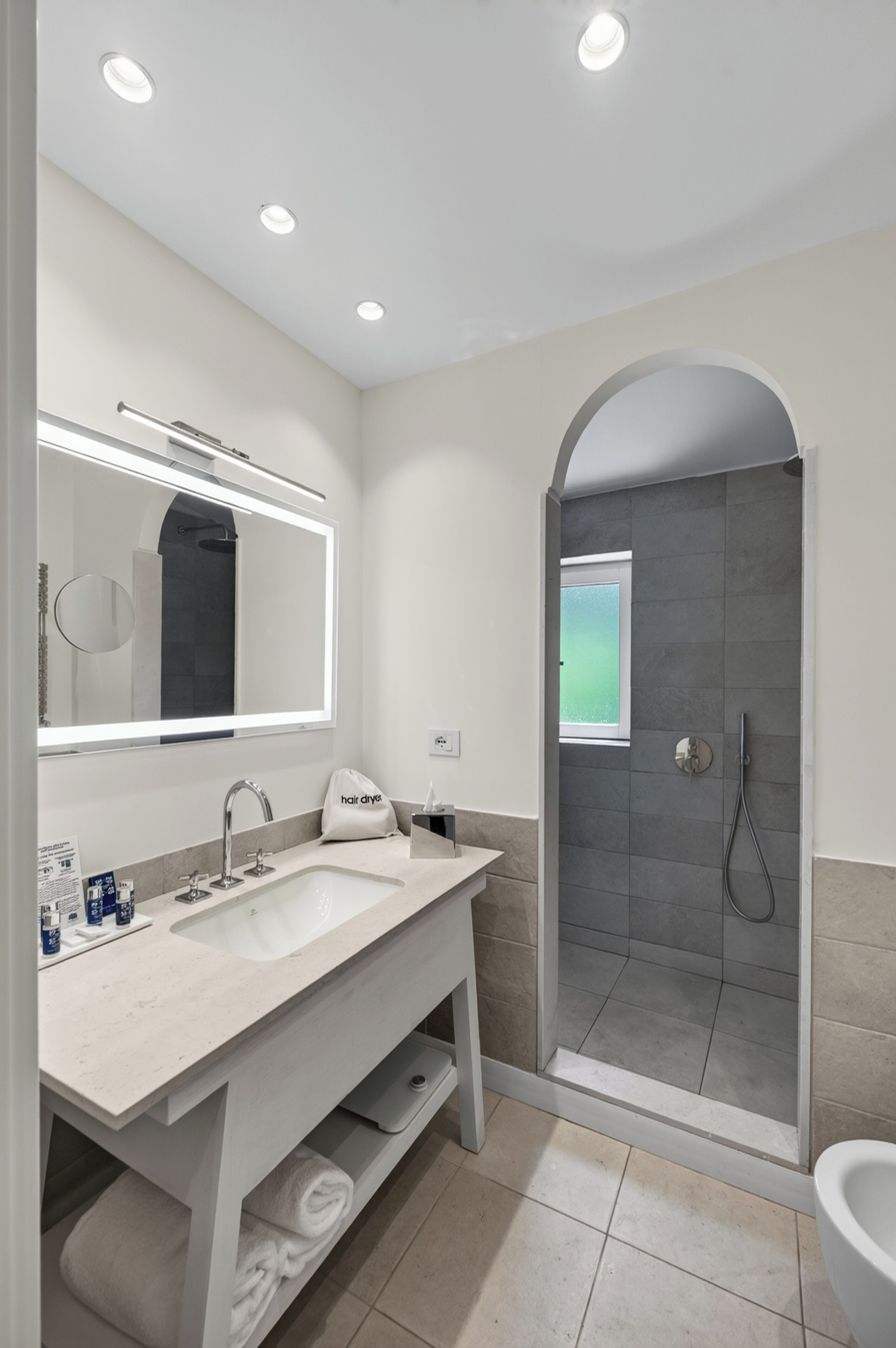 A modern bathroom with a double sink vanity, a large mirror, a towel rack, and a shower area with a glass door.