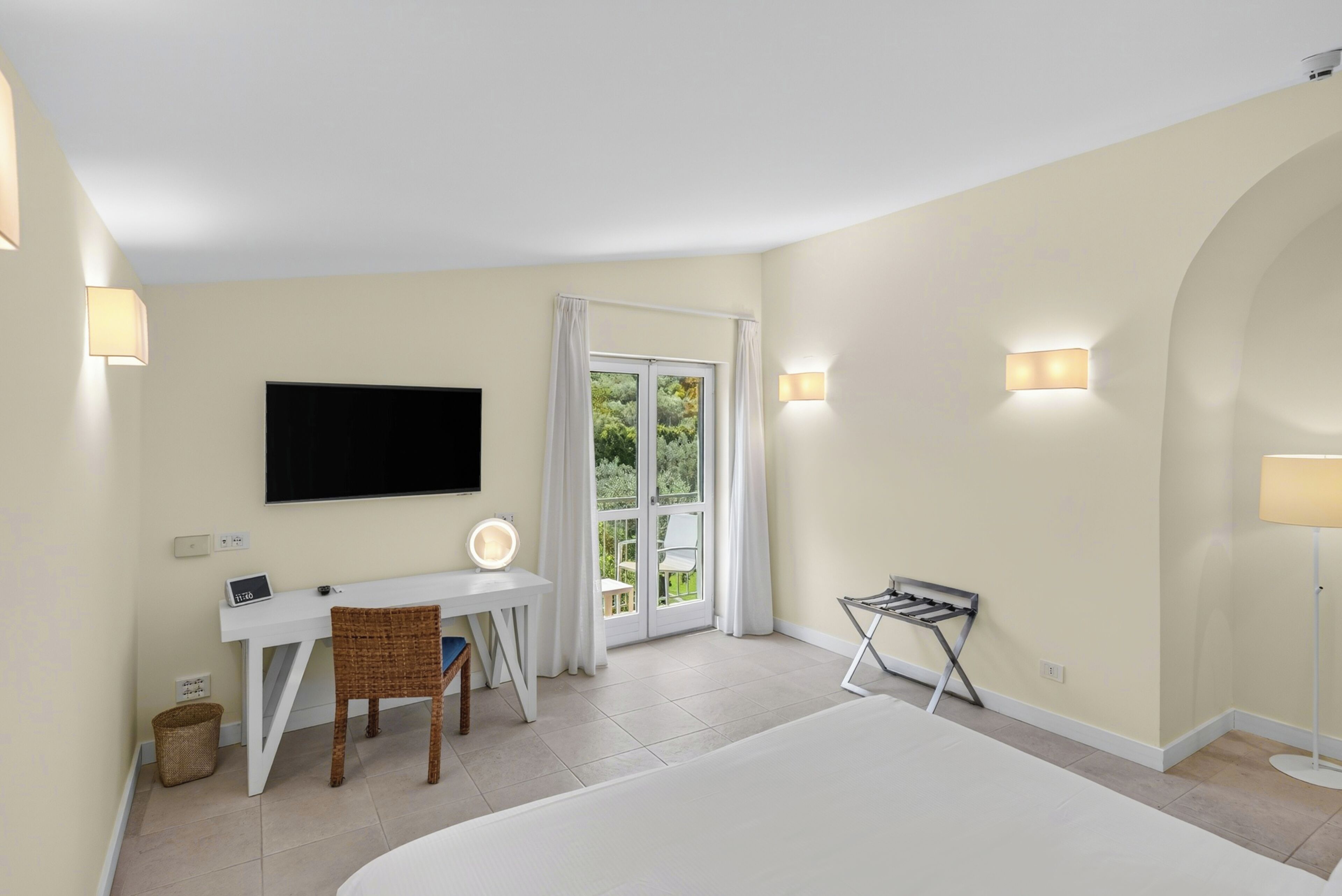 A hotel room with a bed, a desk with a chair, a television, and a window with curtains.