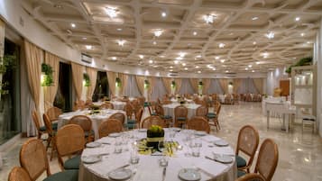 A banquet hall with round tables set for dining, featuring a central floral arrangement.