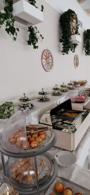 A buffet setup with various food items, including pastries and a hot dish, arranged on a table with decorative plates and hanging plants. - Grand Hotel Aminta  (Sorrento)