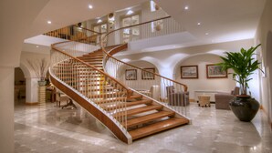A spacious interior with a wooden spiral staircase, a large potted plant, and a well-lit living area with seating. - Grand Hotel Aminta  (Sorrento)