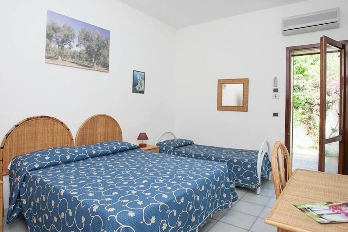 Un dormitorio con dos camas, una mesita, una silla, un espejo y un equipo de aire acondicionado.