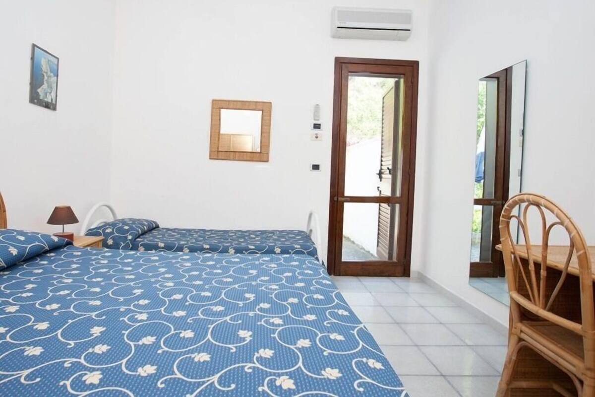 Un dormitorio con una cama, una silla, un espejo y un equipo de aire acondicionado.