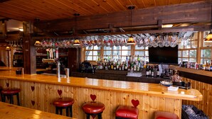 A bar area with wooden bar counter, stools with heart-shaped cutouts, and a variety of bottles and glasses. - Alpenhof (Teton Village)