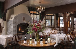 A dining room with round tables, chairs, a fireplace, and a chandelier. - Alpenhof (Teton Village)