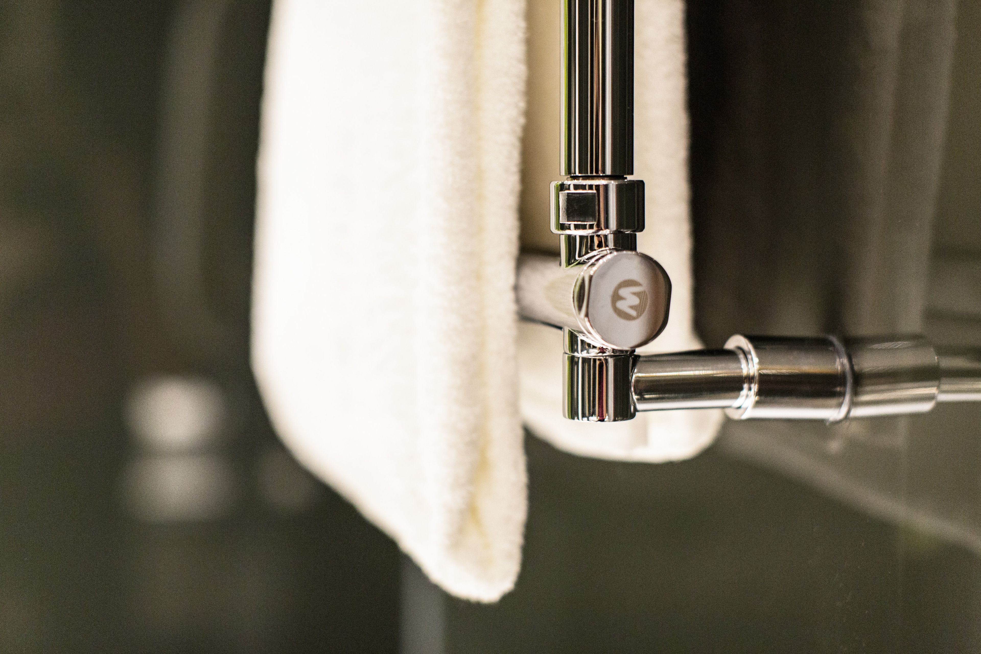A close-up of a metallic faucet with a lever handle, attached to a white towel hanging from a metal rod.