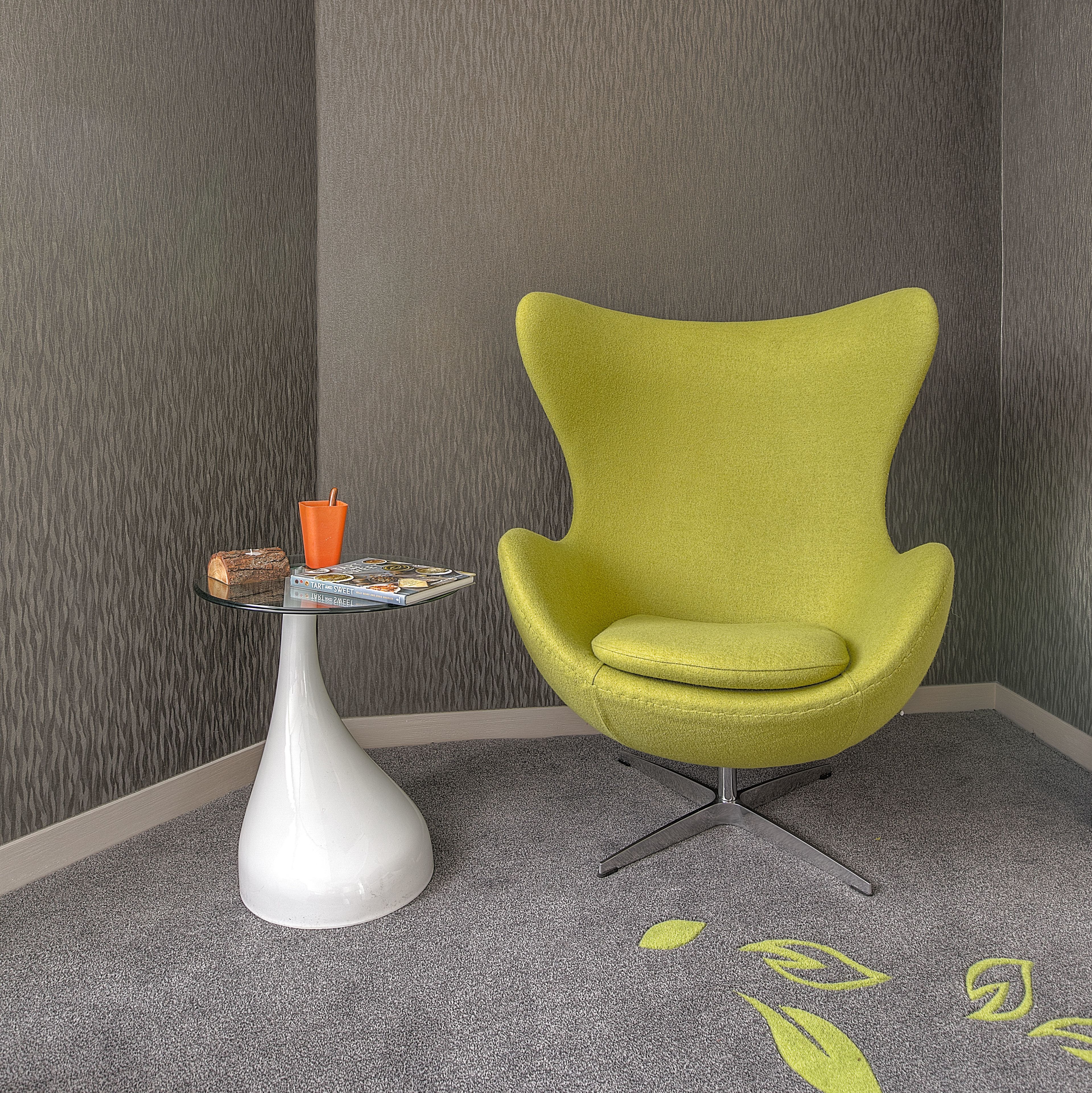 A modern room with a green armchair, a white vase, and a small table with a book and a candle.
