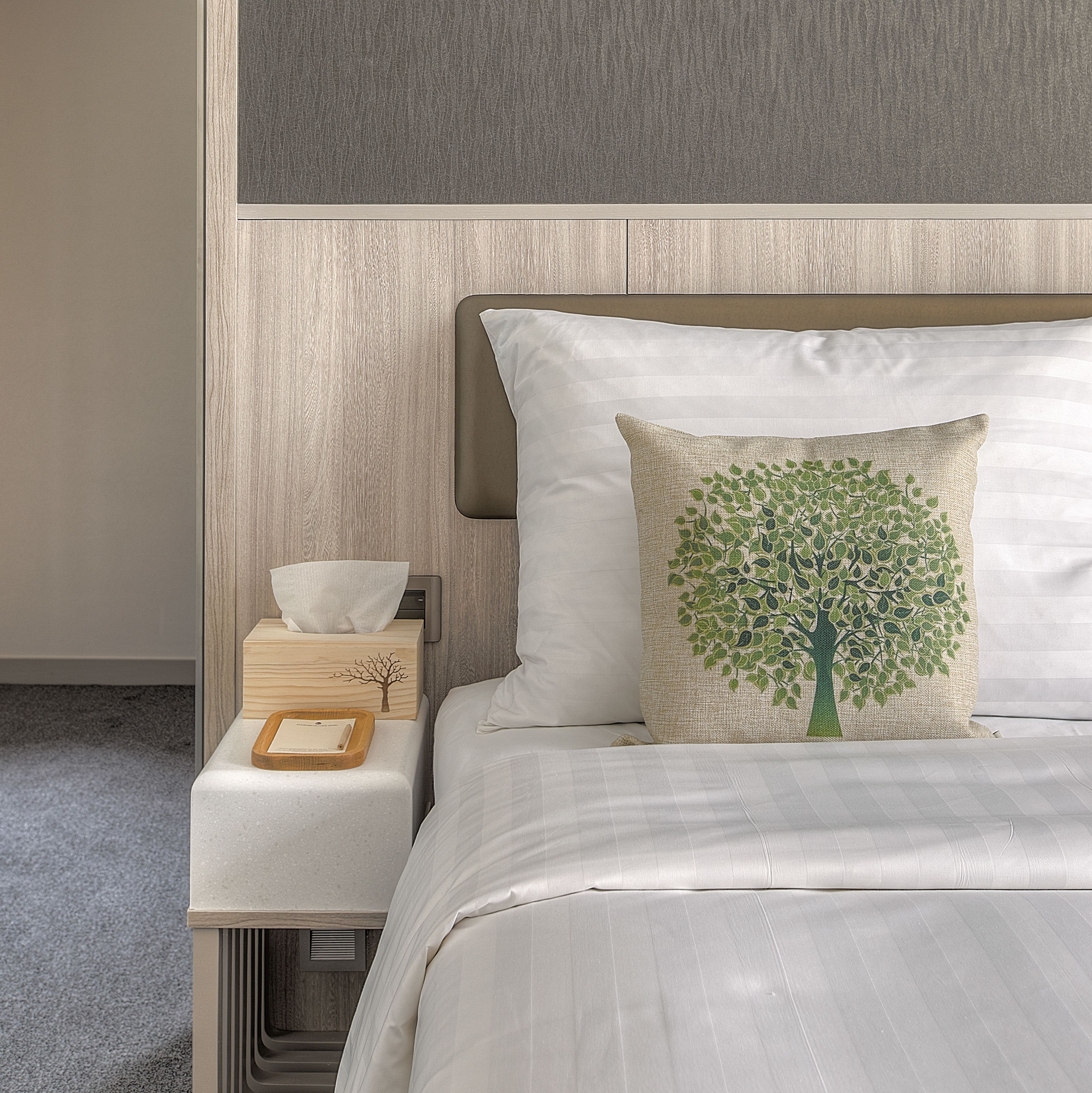 A neatly made bed with a white pillow and a decorative pillow with a tree design.