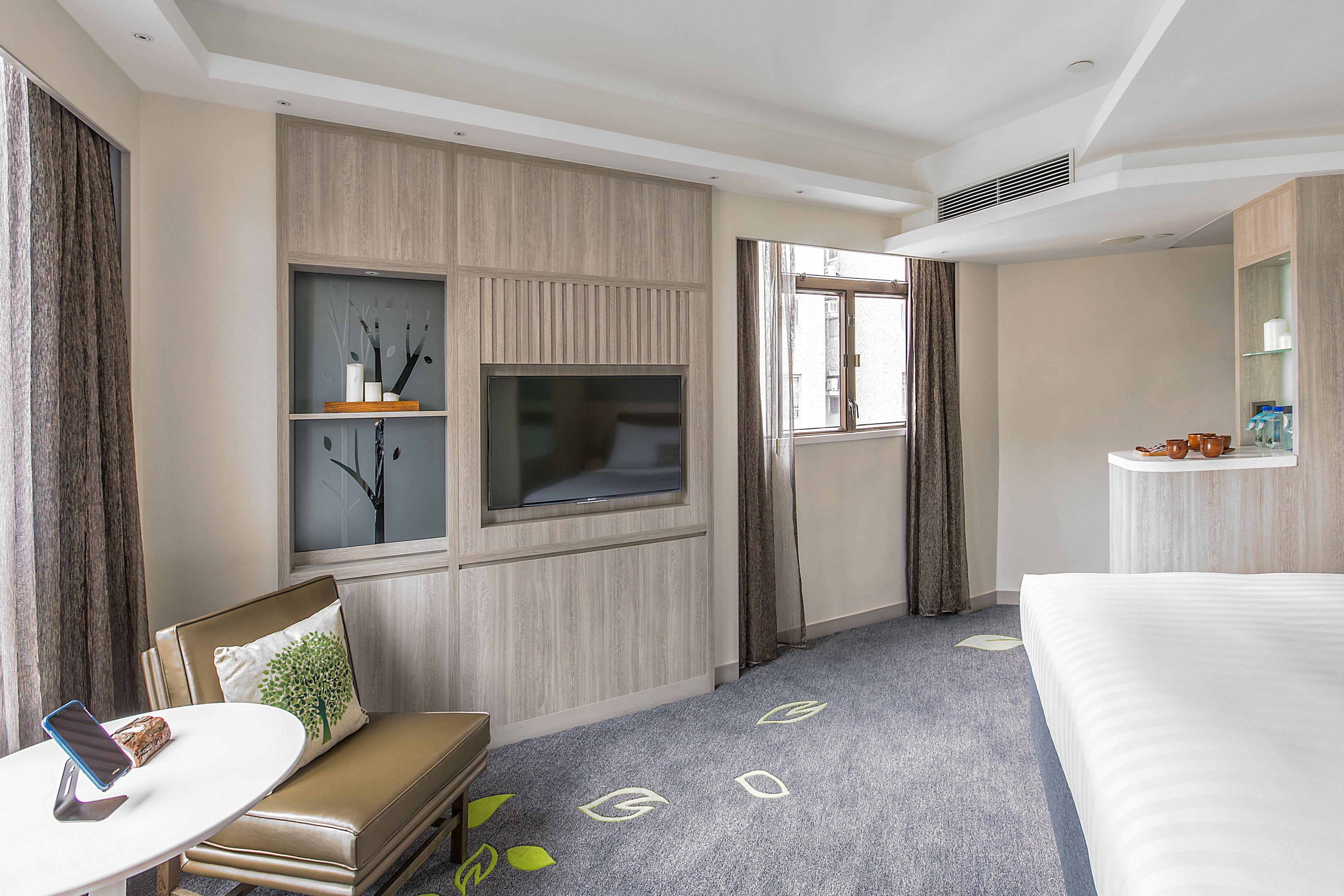 Hotelkamer met een bed, een aan de muur bevestigde televisie, een zithoek met een tafel en een groot raam.