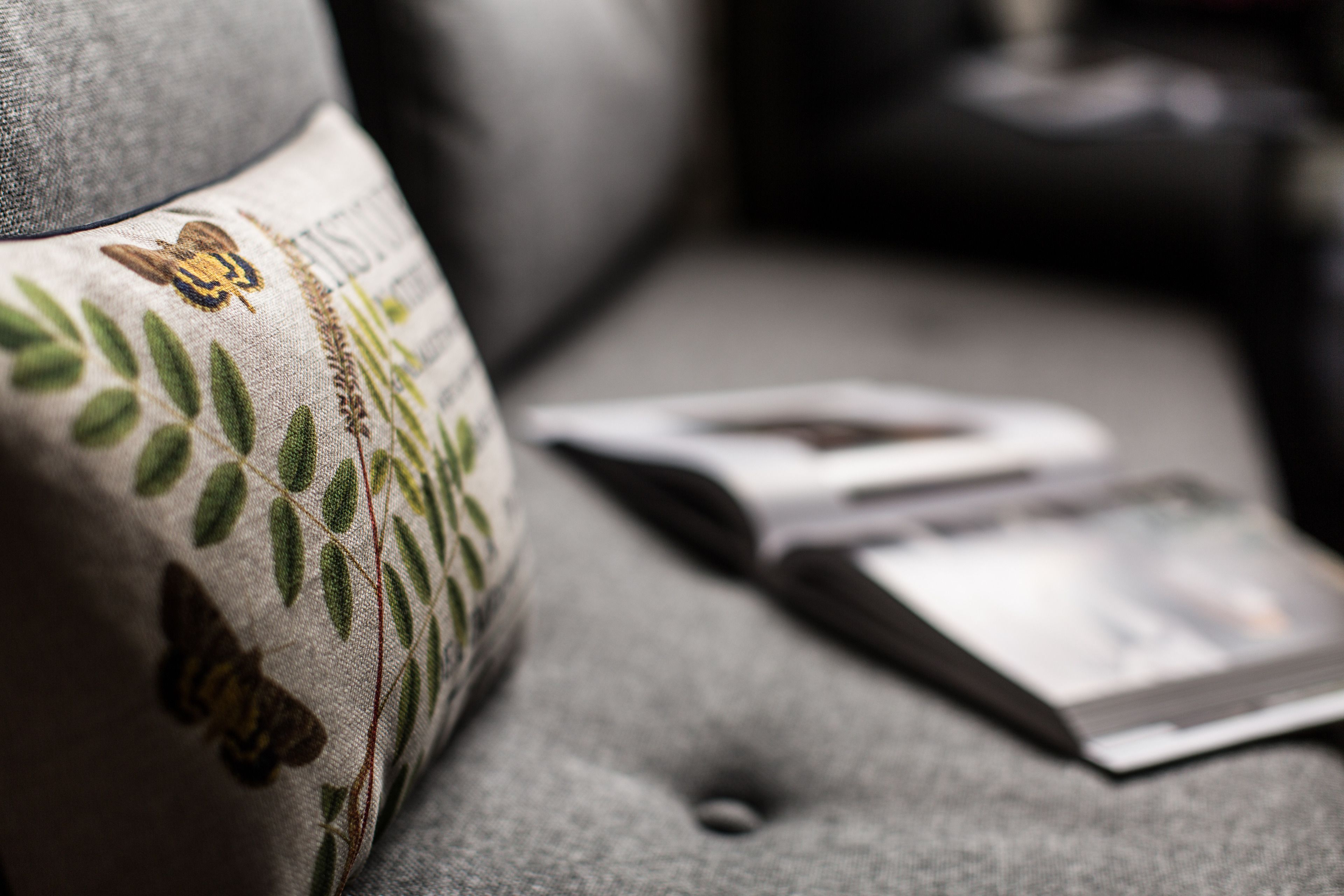 A close-up of a grey upholstered sofa with a floral pattern and a magazine on it.