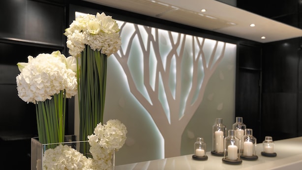 A reception area with a modern design, featuring a white reception desk, a glass vase with white flowers, and a wall with a tree silhouette. - Stanford Hillview Hotel (Kowloon)
