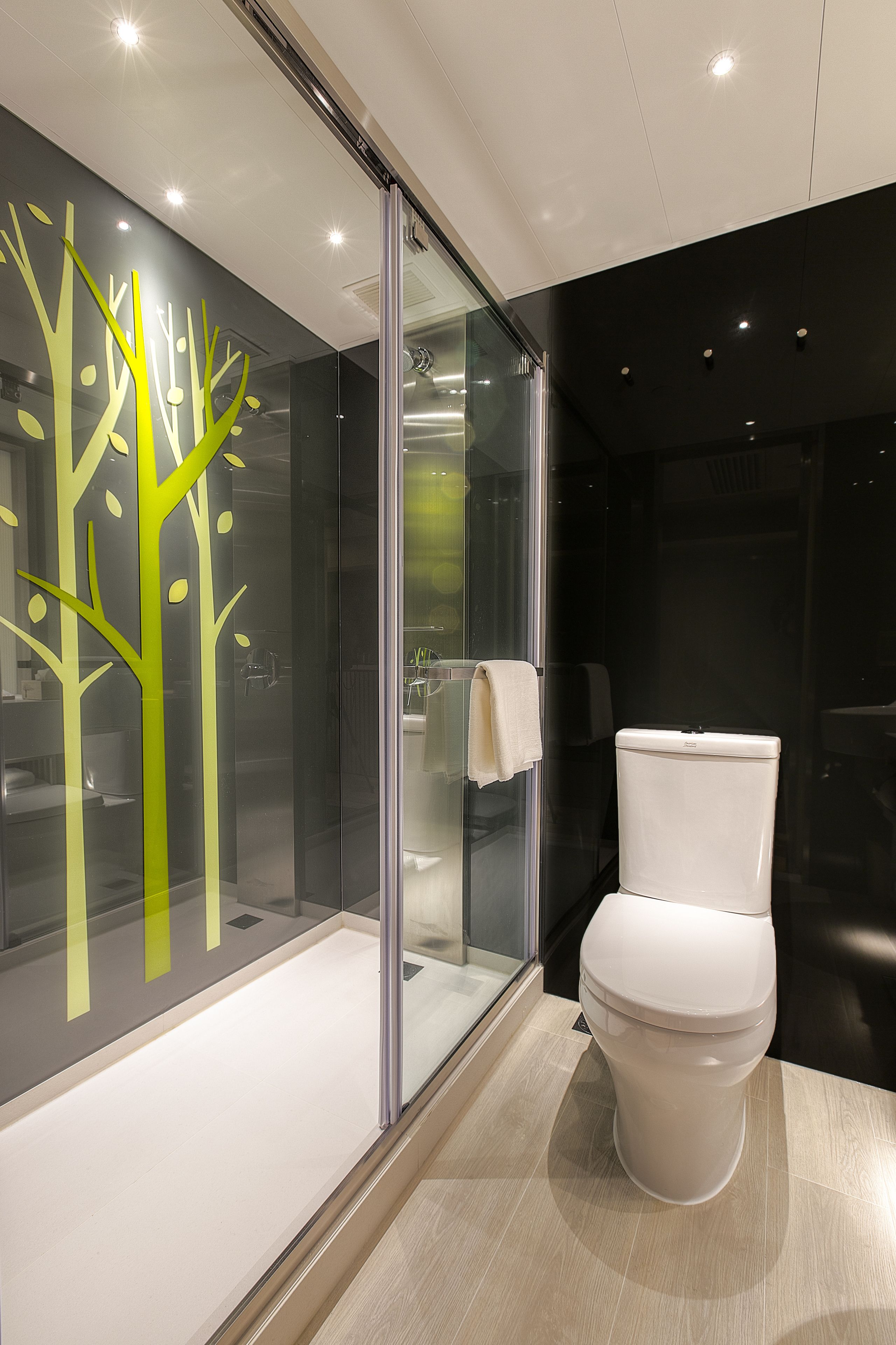 Un baño moderno con inodoro, cabina de ducha de vidrio y una pared con diseños abstractos de árboles.