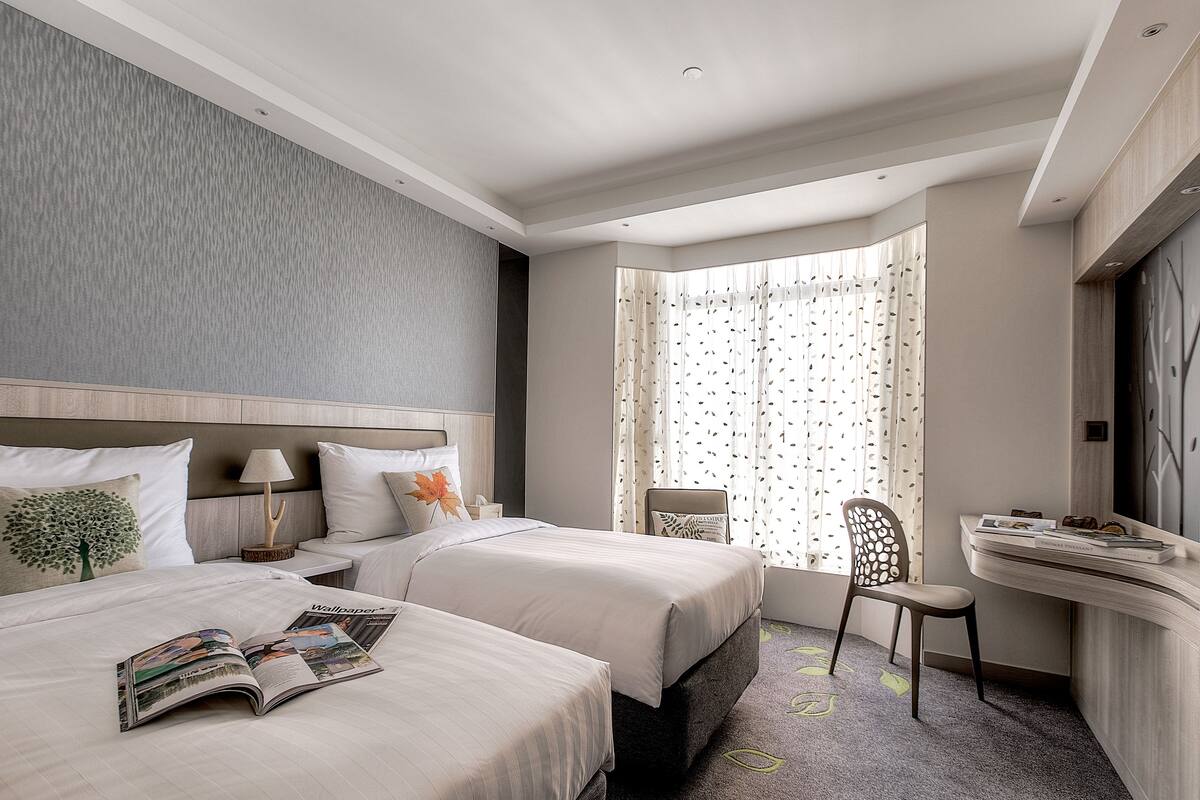 A hotel room with two beds, a desk, and a chair.