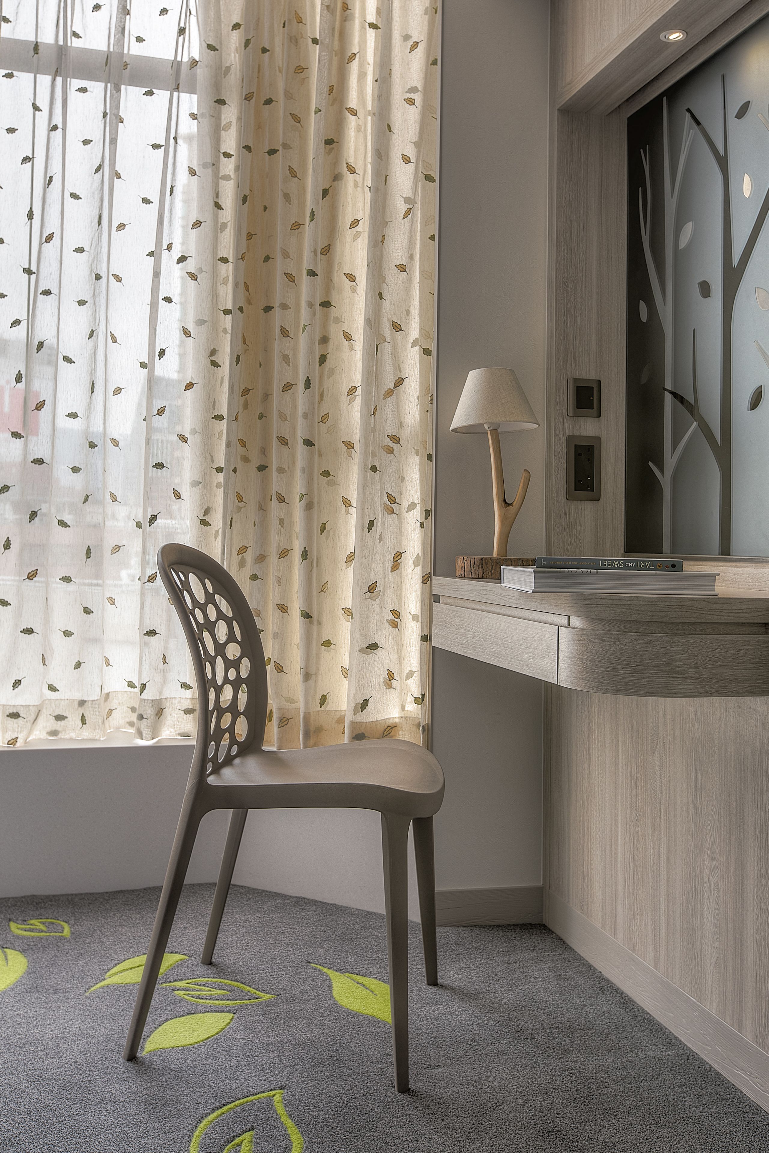 Une chambre moderne équipée d’un bureau, d’une chaise et d’une fenêtre ornée de rideaux légers.