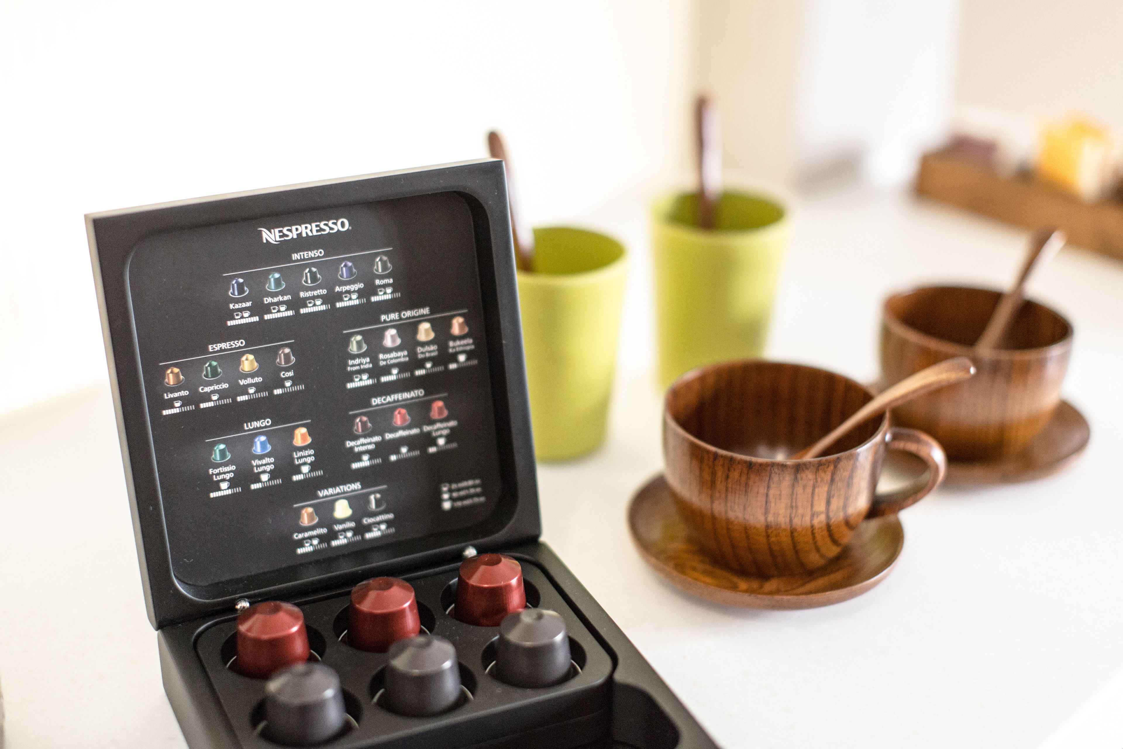 Una máquina de café Nespresso con un manual, rodeada de tazas de madera y una taza verde.