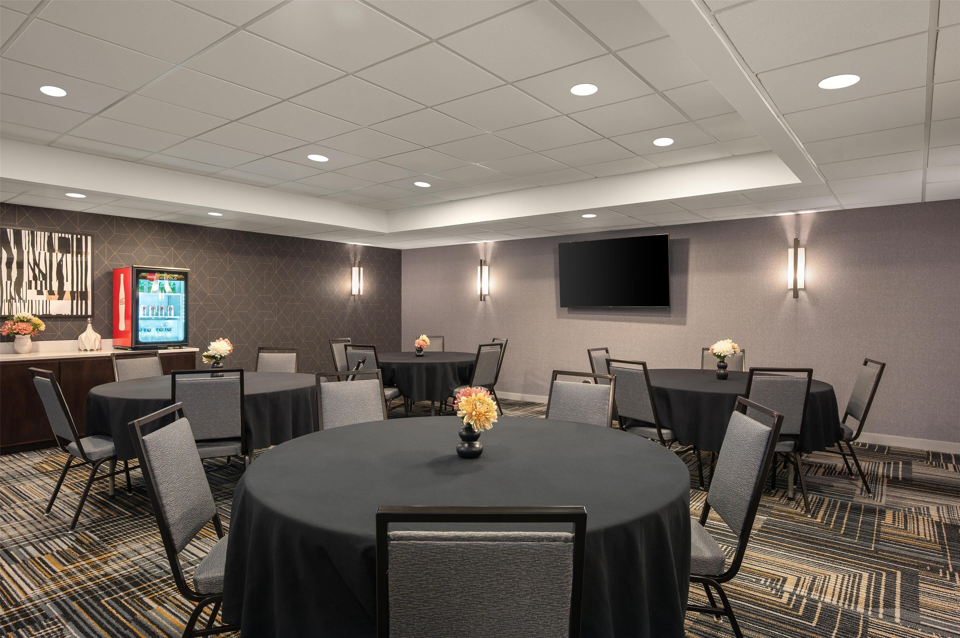 A conference room with round tables, chairs, a flat-screen TV, and wall-mounted lights.