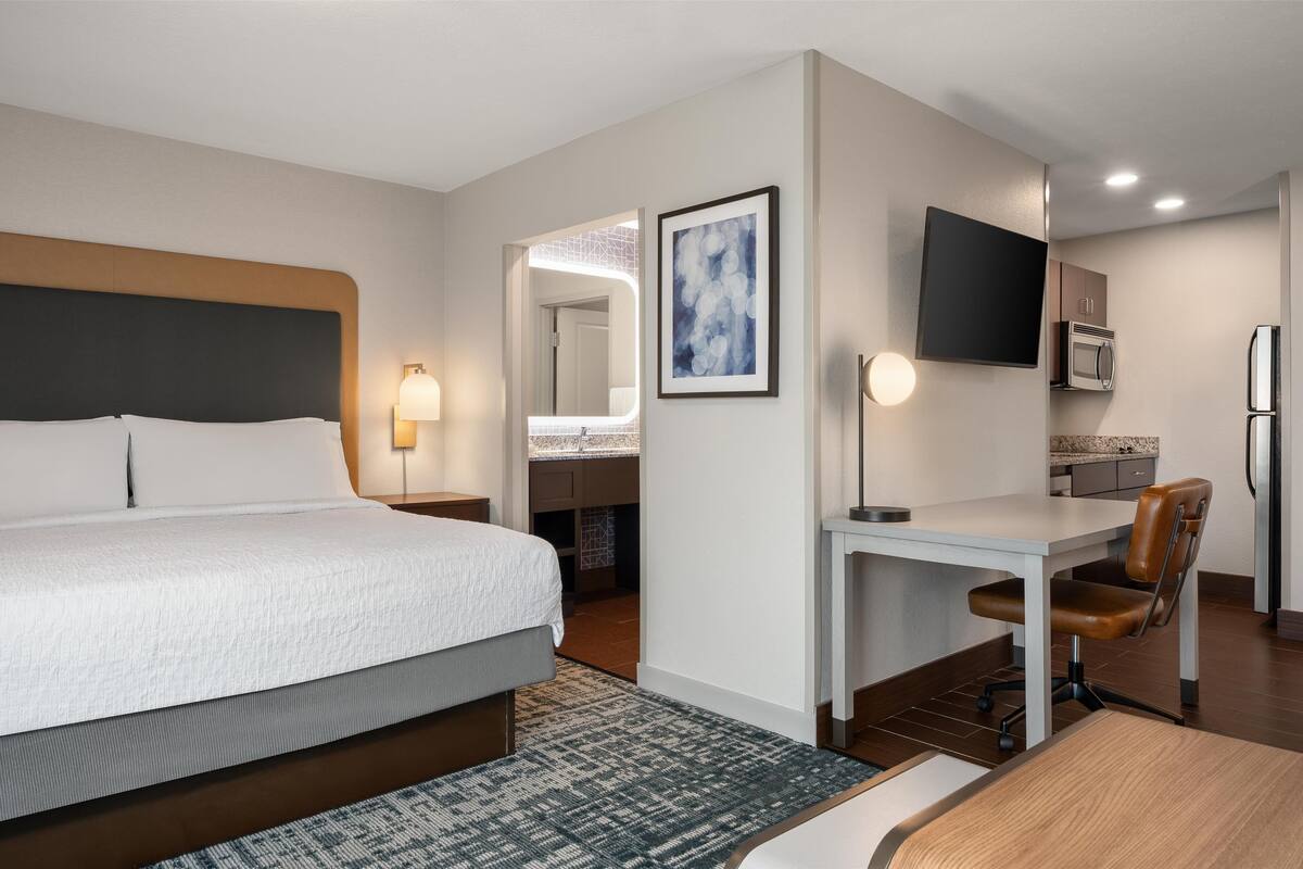 Camera d'albergo con letto, scrivania, sedia, televisore e angolo cottura.