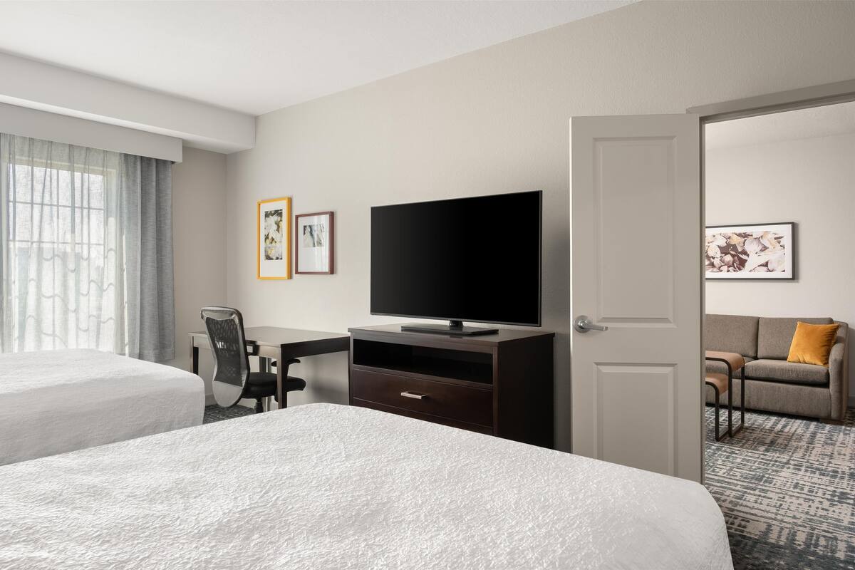 Una camera d'albergo con due letti, una scrivania con televisore a schermo piatto e un divano con un cuscino.