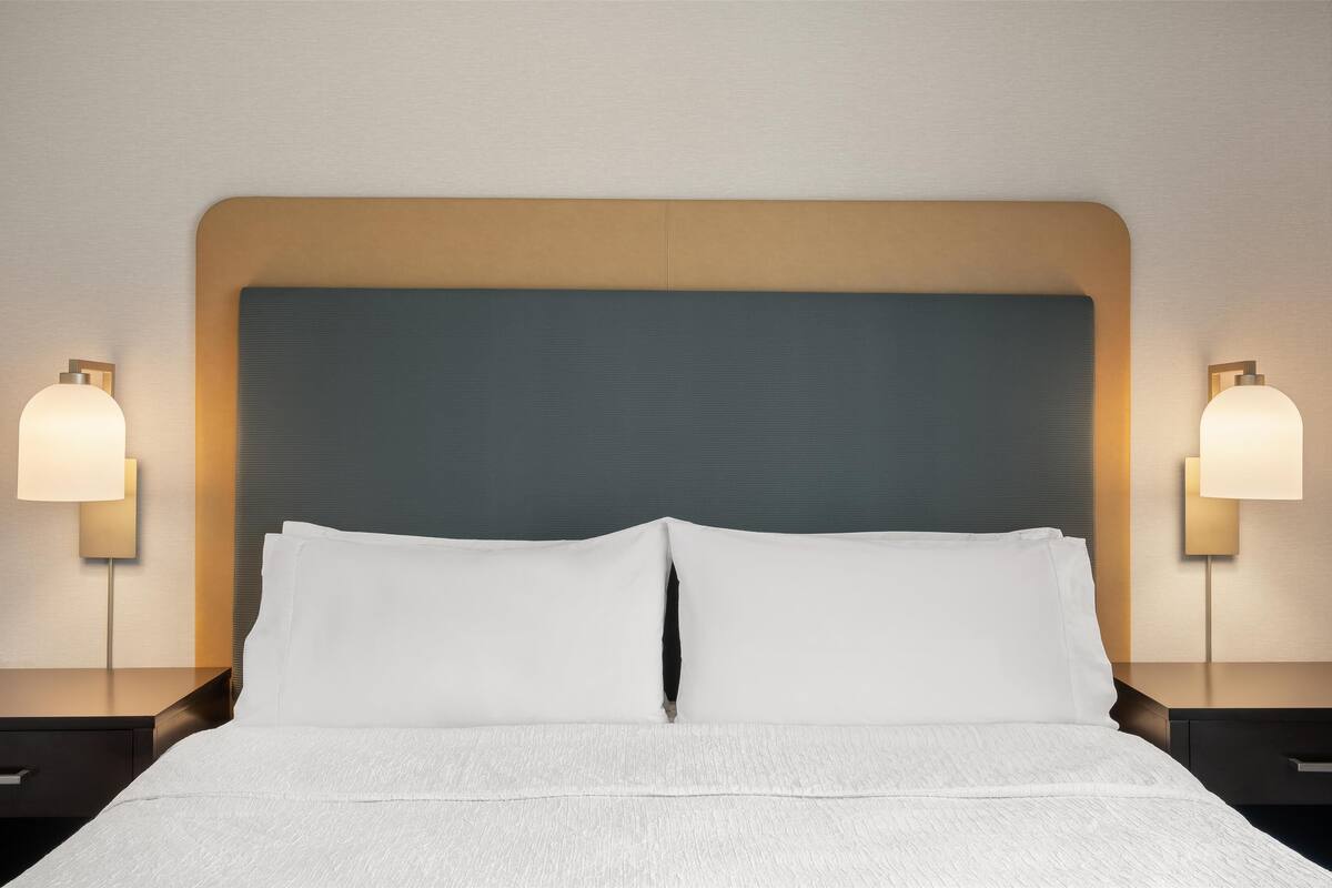 Un letto rifatto con lenzuola bianche, una testiera in legno e due abat-jour.