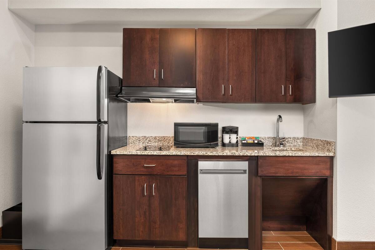 Una cucina compatta con pensili in legno scuro, un frigorifero in acciaio inossidabile, un forno a microonde ed una lavastoviglie.