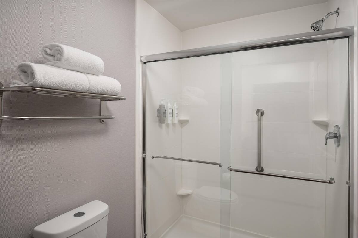 Un bagno moderno con cabina doccia in vetro, un water e un portasciugamani con asciugni piegati.