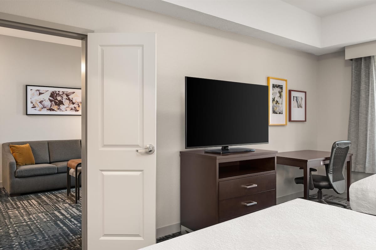 Una camera d'albergo con un letto, una scrivania con una sedia, un televisore, un divano con un cuscino e quadri appesi al muro.
