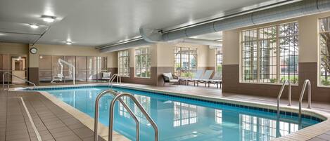 An indoor swimming pool with clear water, surrounded by lounge chairs and a tiled floor.