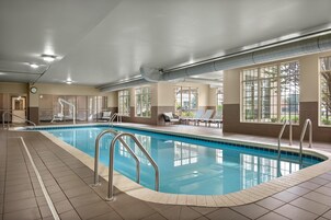 Piscina interior com água cristalina, rodeada por espreguiçadeiras e chão revestido de azulejos.
