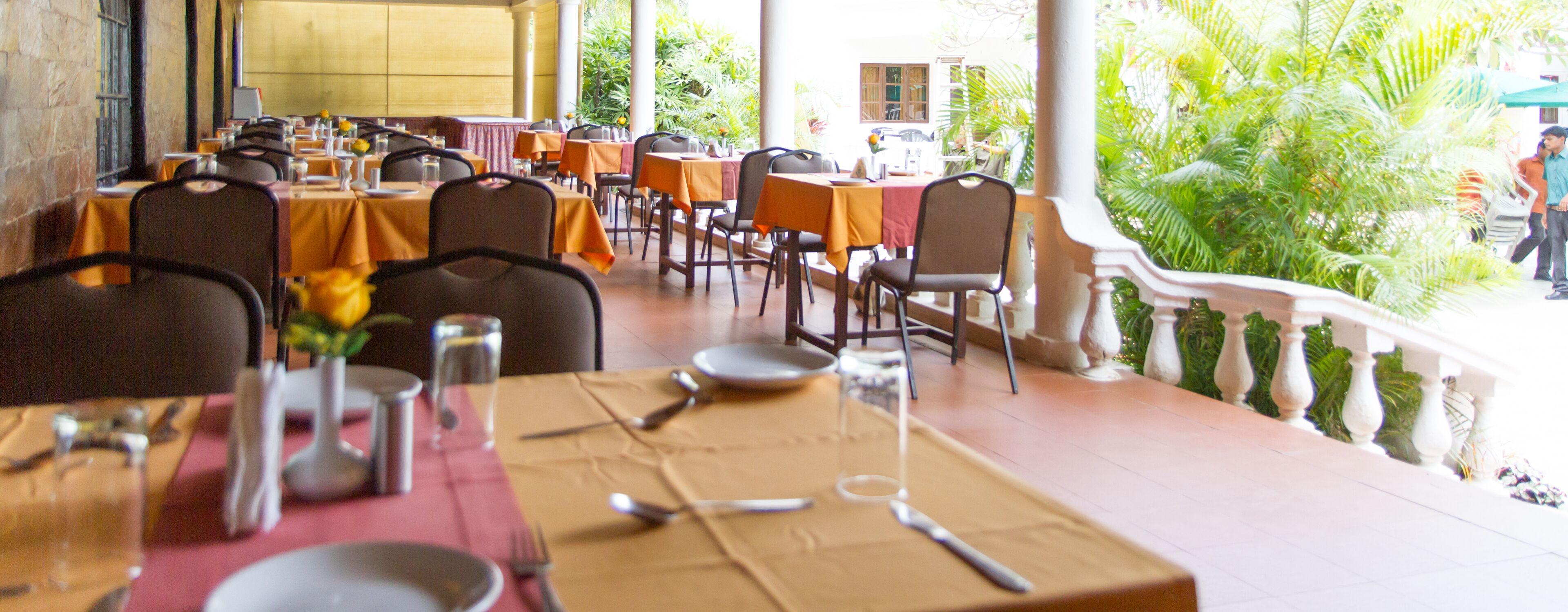 An outdoor restaurant with tables set for dining, surrounded by greenery and a balcony railing.