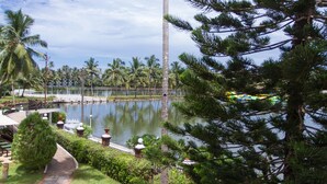 A serene lakeside view with palm trees, a pathway, and a distant building. - Resorte Marinha Dourada (Arpora)