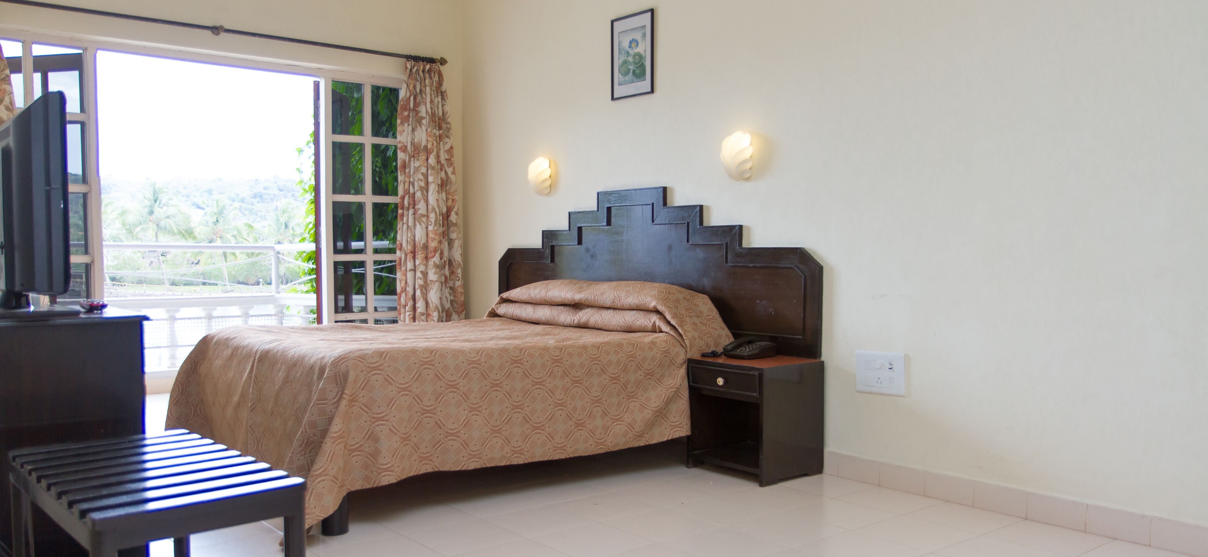 A bedroom with a bed, a nightstand, a desk with a chair, and a window with curtains.
