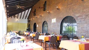 A restaurant with multiple tables, each set with chairs and tablecloths, featuring a brick wall and arched windows. - Resorte Marinha Dourada (Arpora)