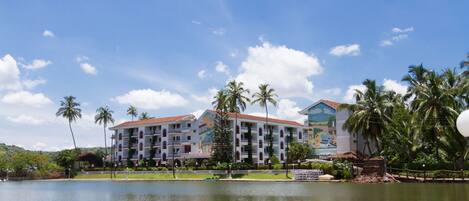 A hotel with multiple balconies, a swimming pool, and palm trees.
