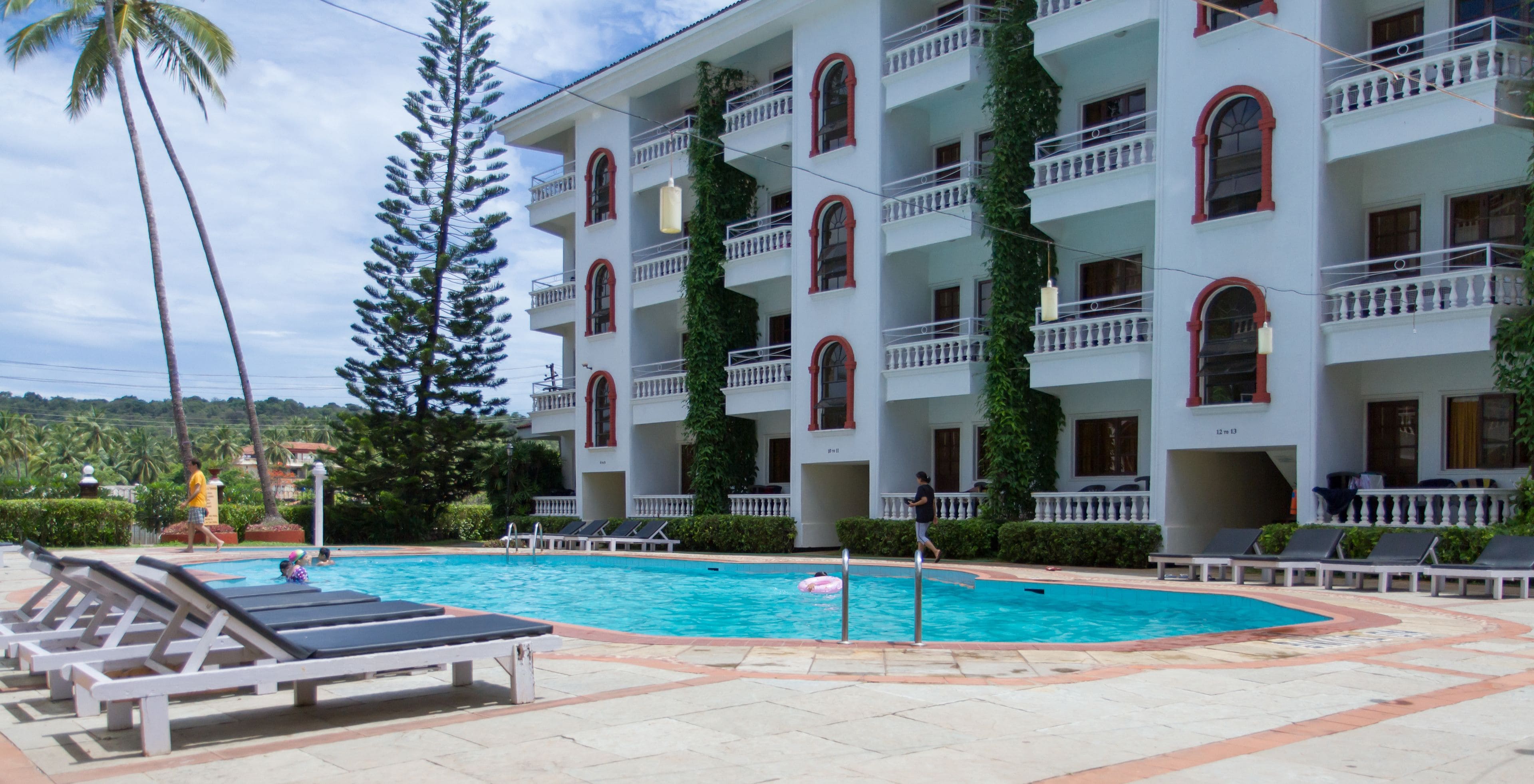A hotel with a swimming pool, lounge chairs, and a multi-story building with balconies.