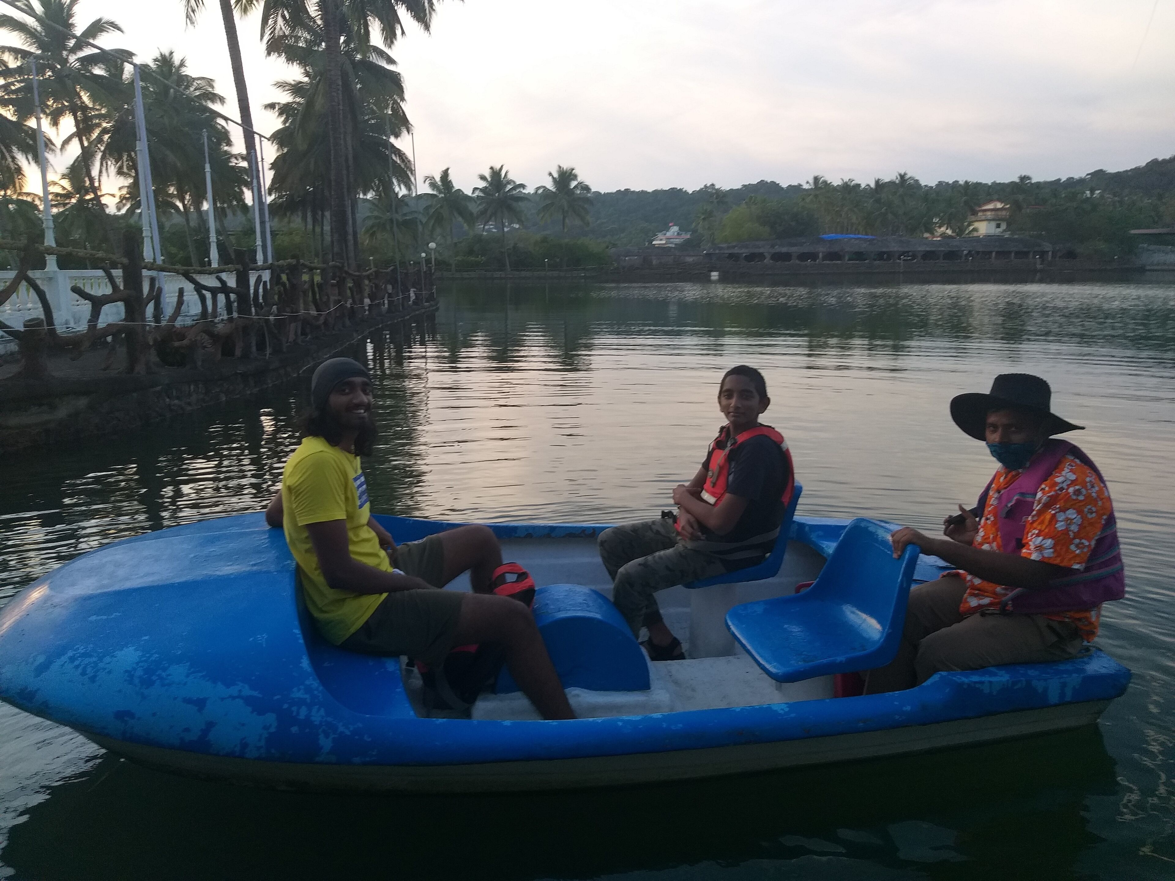 Tres personas en un bote inflable azul con barandilla, rodeadas de agua tranquila y palmeras.
