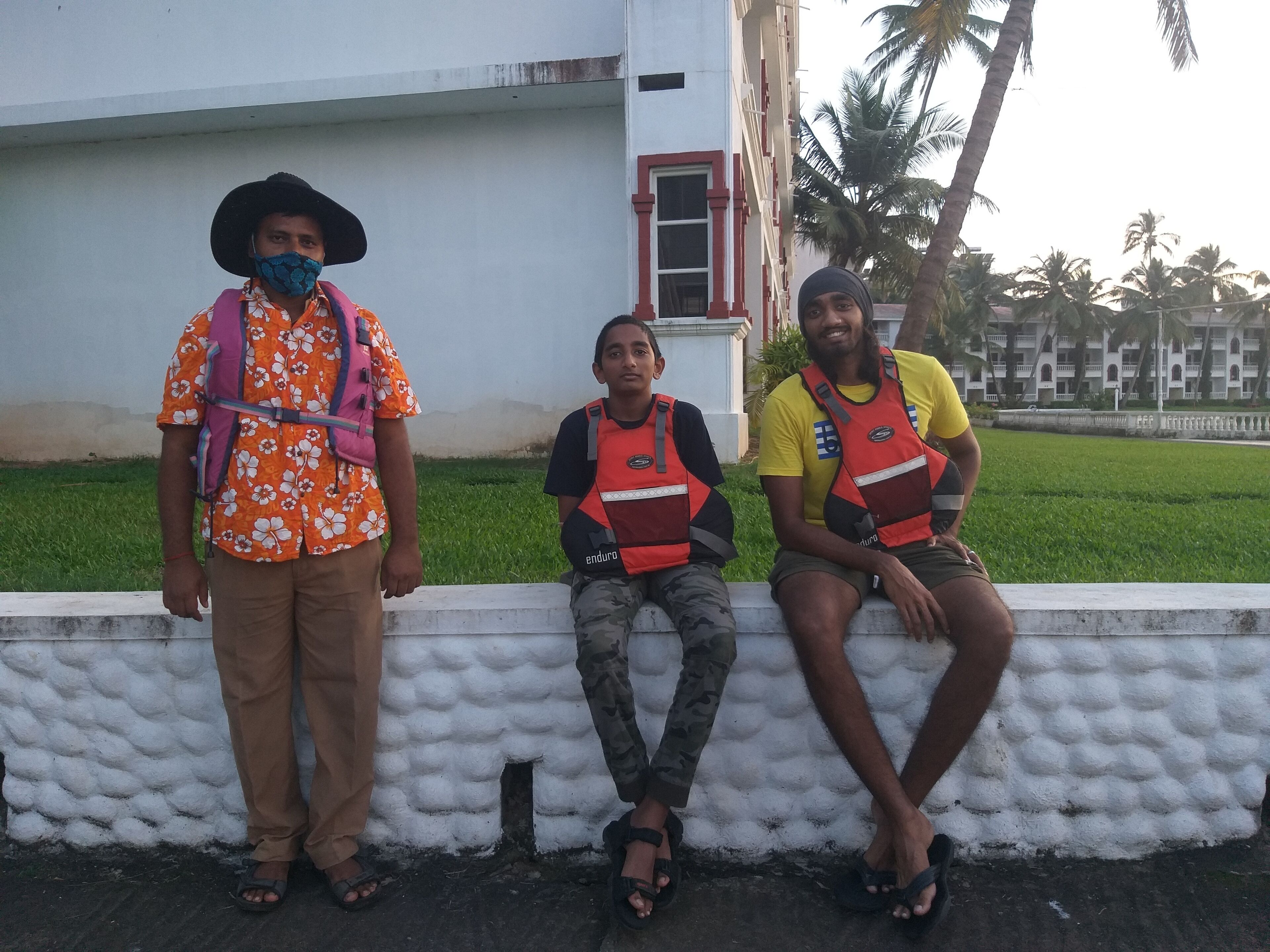 Three individuals sitting on a white wall with a building in the background.