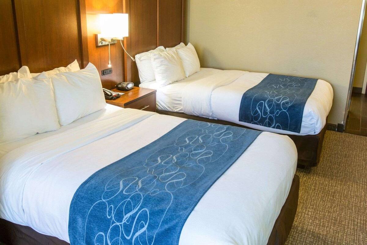 A hotel room with two beds, a nightstand, a lamp, and a wooden headboard.