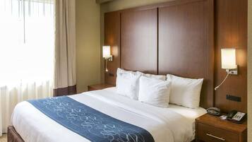 A hotel room with a large bed, two bedside tables, a nightstand, a lamp, and a phone.