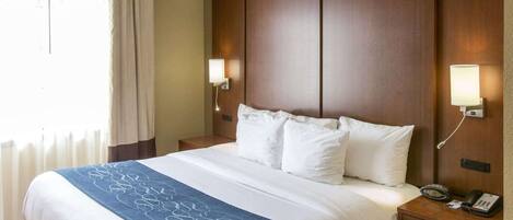 A hotel room with a large bed, two bedside tables, a nightstand, a lamp, and a phone.