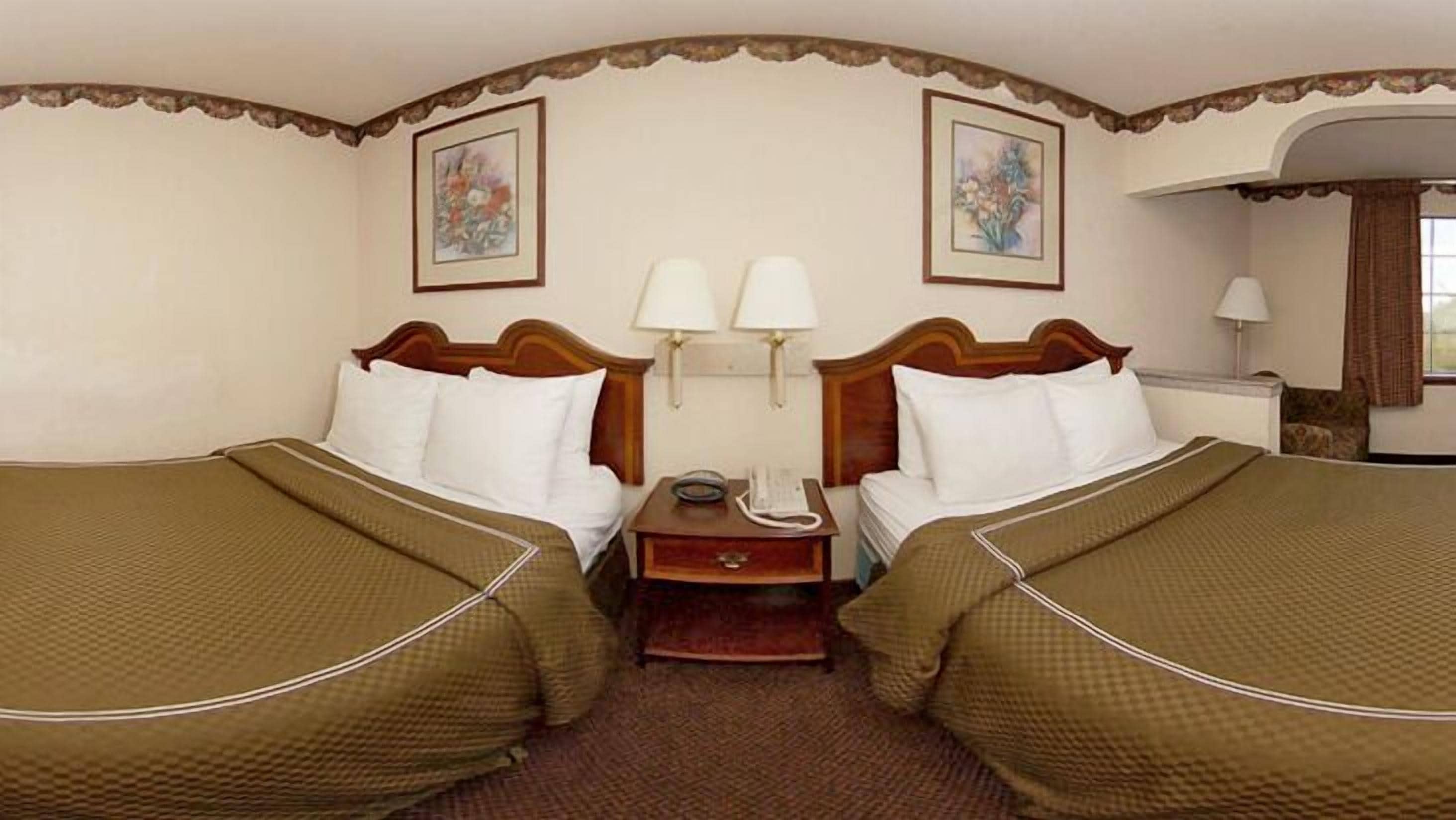 A hotel room with two beds, a nightstand with a lamp, and two framed pictures on the wall.