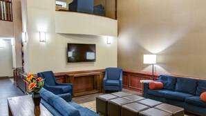 A hotel lobby with a high ceiling, a flat-screen TV mounted on the wall, and a seating area with sofas and a coffee table. - Comfort Suites Idabel (Idabel)