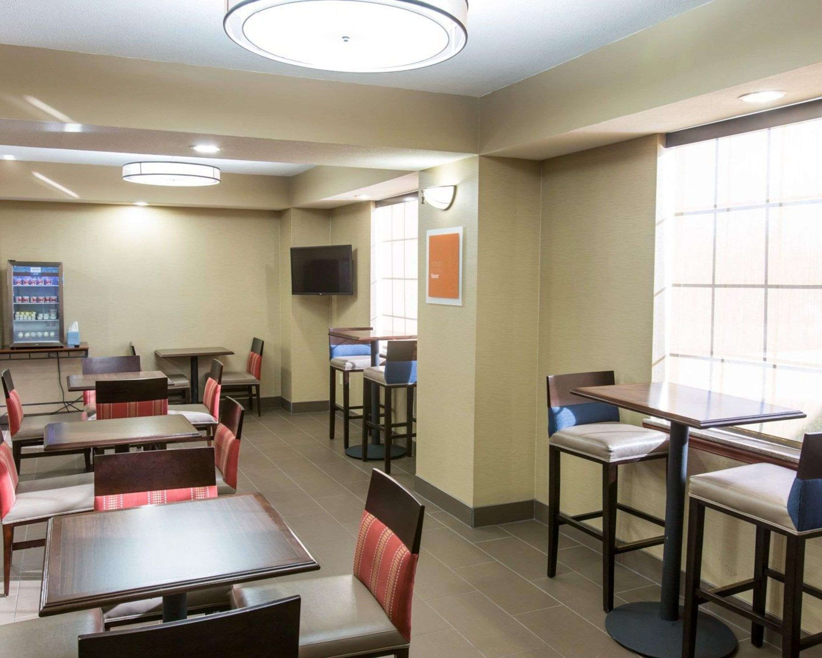 A hotel room with a dining area featuring tables and chairs, a flat-screen TV mounted on the wall, and a vending machine.