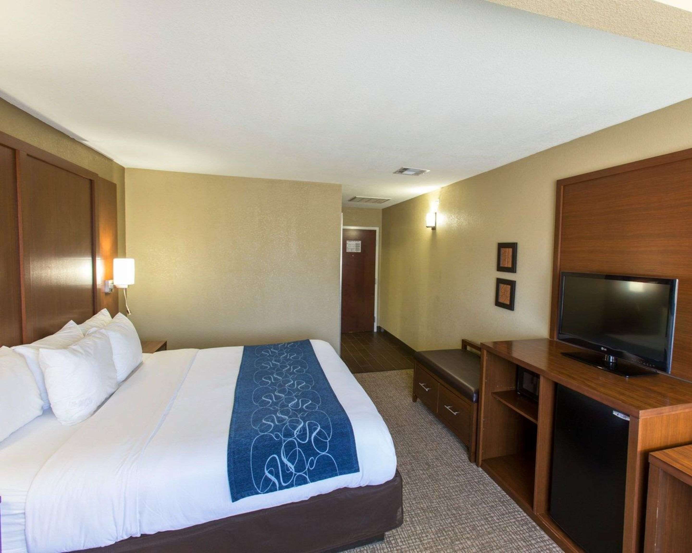 A hotel room with a bed, a TV, a desk, and a wall-mounted TV.