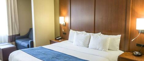 Ein Hotelzimmer mit einem großen Bett, einem Schreibtisch, einem Stuhl und einem Nachttisch mit Lampe.