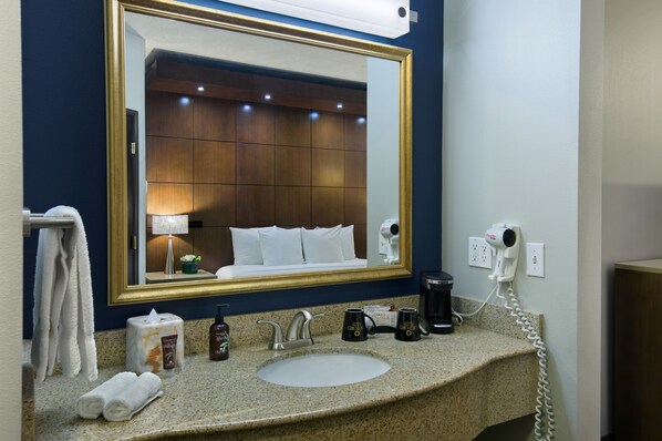 A hotel bathroom with a large mirror, a sink, a hairdryer, and toiletries. - Oxford Suites Downtown Spokane (Spokane)
